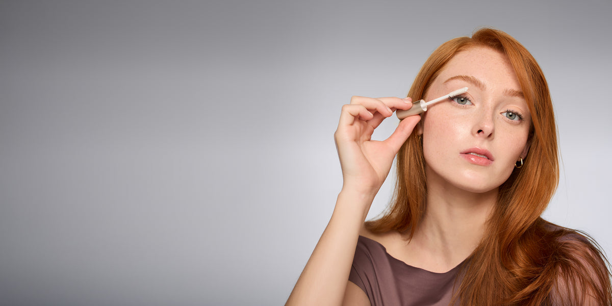 Rothaarige Frau trägt mit einem Applikator einen Lash Conditioner von jane iredale auf ihre Wimpern auf.