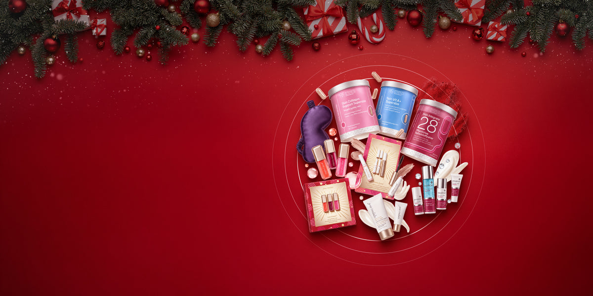 Weihnachtliches Werbemotiv mit schwebenden Hautpflege-, Make-up- und Nahrungsergänzungsprodukten von Environ, jane iredale und Advanced Nutrition Programme vor rotem Hintergrund, eingerahmt von Tannenzweigen, Christbaumkugeln und Geschenken.